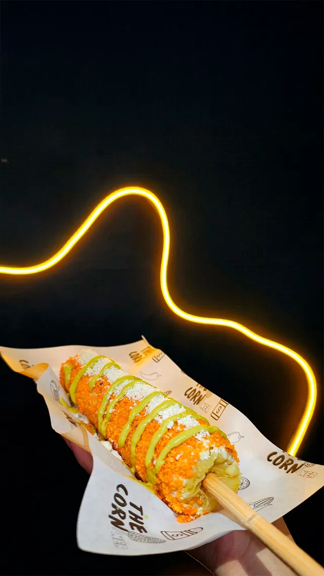 Elote con aderezo verde y polvo de botana sobre papel