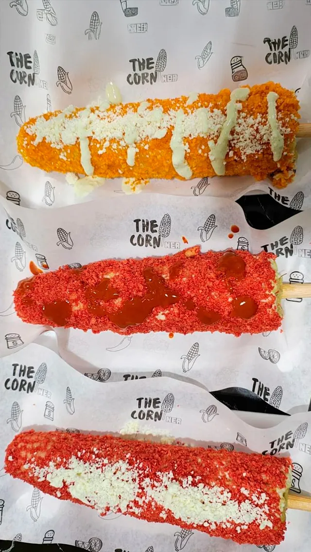 Tres elotes revolcados en papita triturada, con queso y aderezo