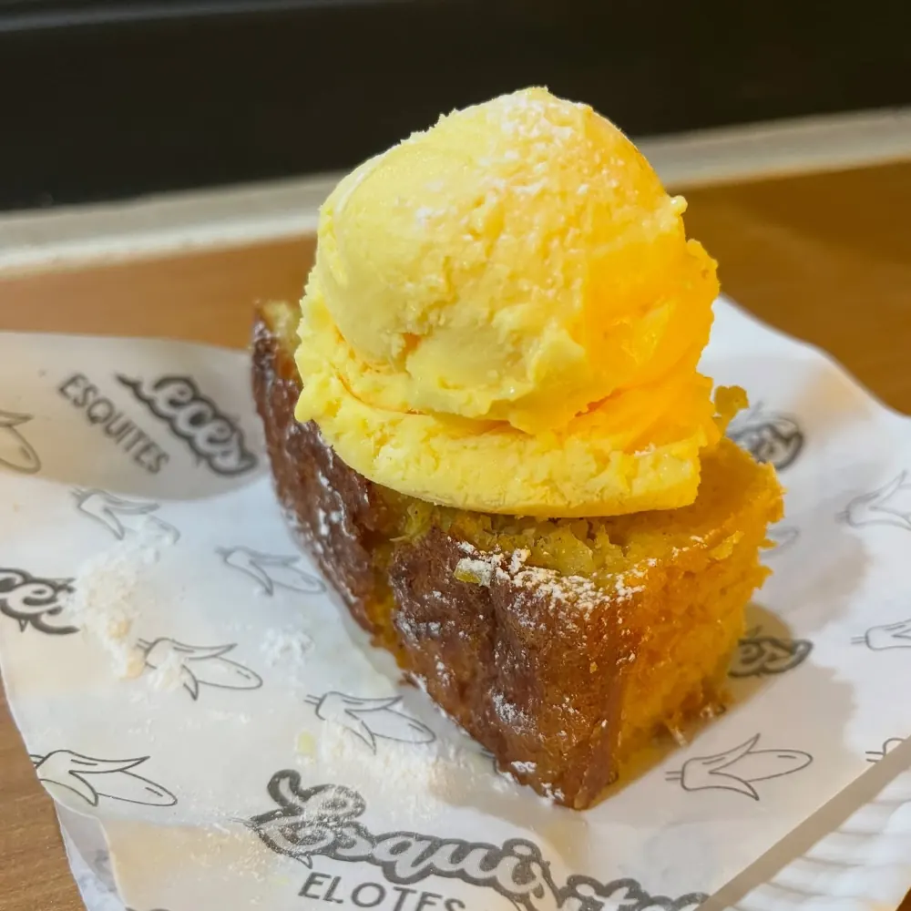 Primer plano de un panqué de elote con una bola de helado amarillo y azúcar glass