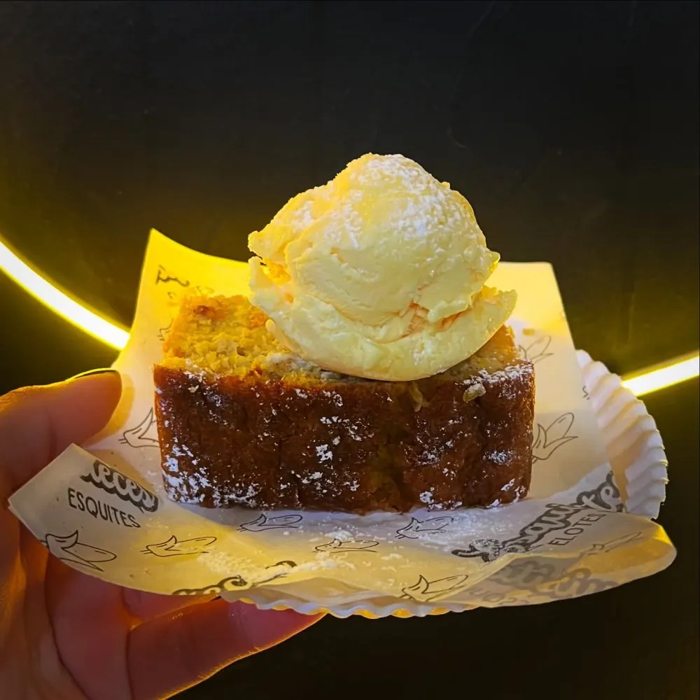 Panqué de elote con una bola de helado y azúcar glass, sobre papel con el logo de Esquisiteces